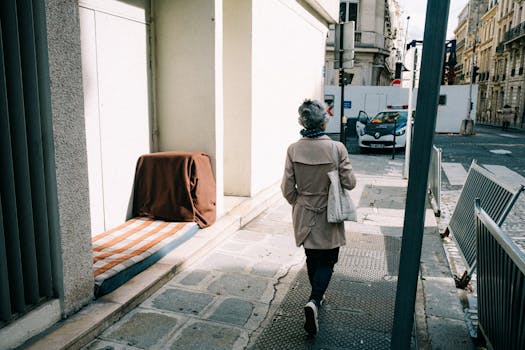 A senior woman walks down a city street in daylight, past buildings and a police car.